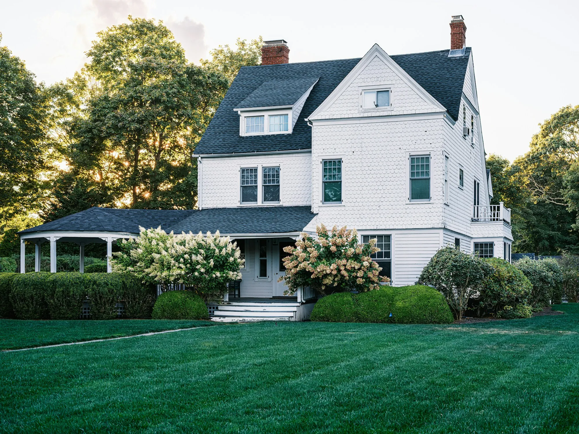 White two-story home with hydrangeas and a lawn